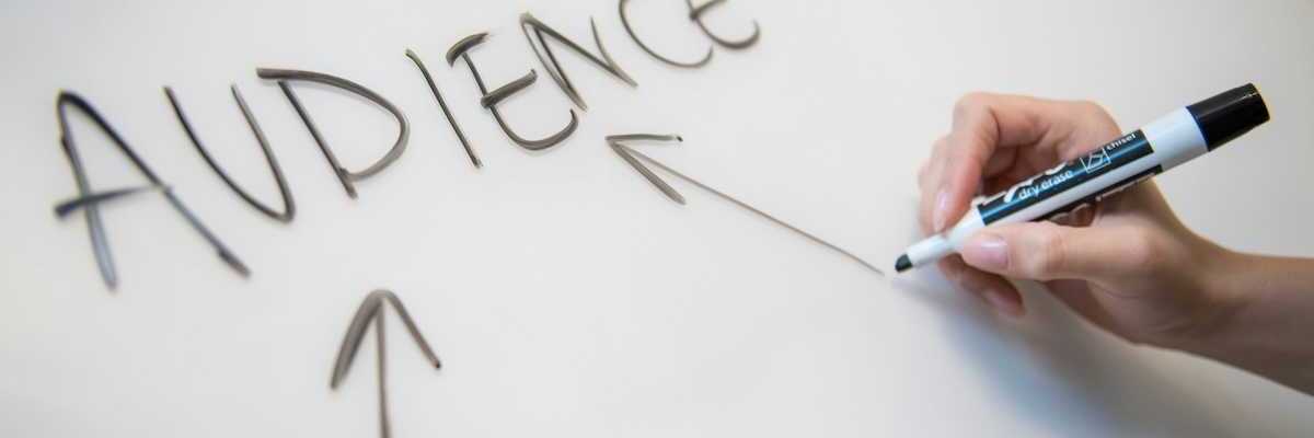 A right hand printing "AUDIENCE" with three arrows on a white board with a black marker