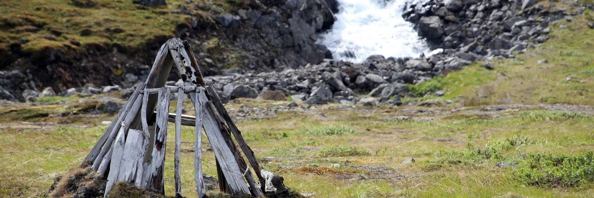 A river running through a green, rocky environment with a small wooden structure in foreground.