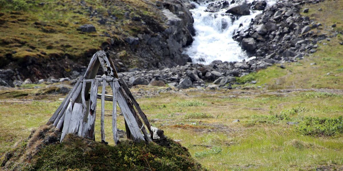 A river running through a green, rocky environment with a small wooden structure in foreground.