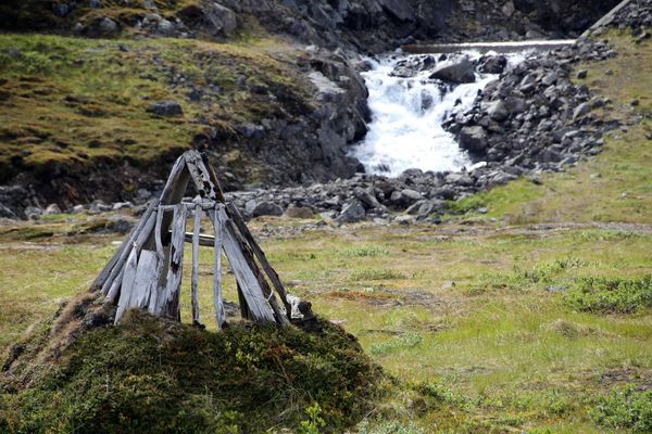 A river running through a green, rocky environment with a small wooden structure in foreground.