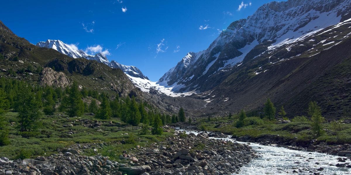 A river running through a lush green mountain valley with a glacier in the background.