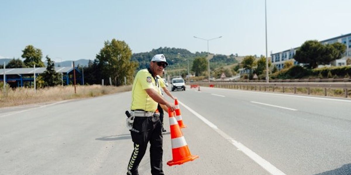 A road safety worker setting orange cones on a highway.