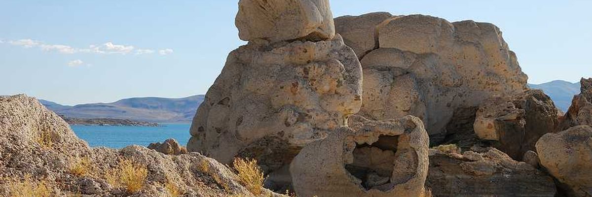 A rock formation in the desert with a lake in the background