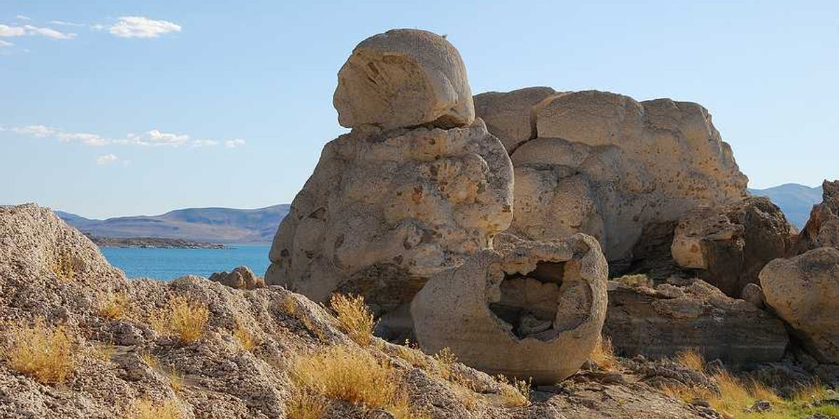 A rock formation in the desert with a lake in the background