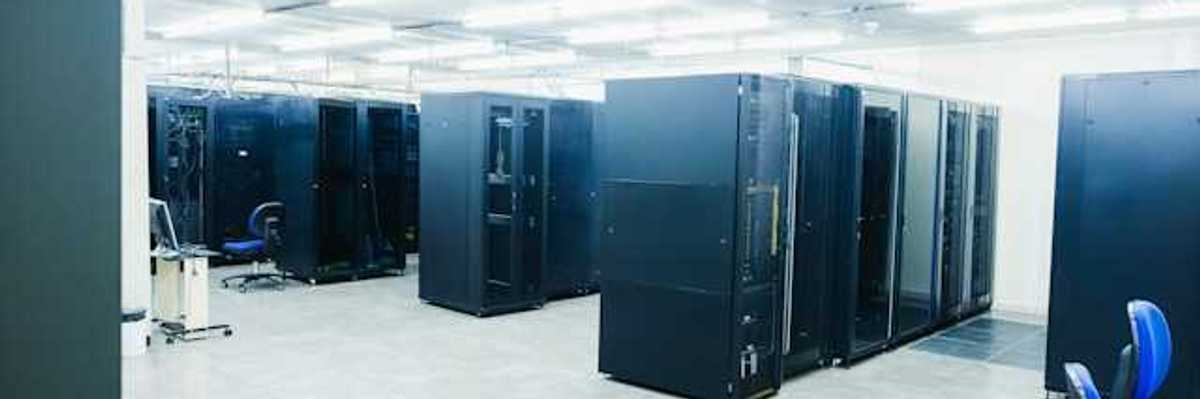 A room full of black server cabinets under fluorescent lighting