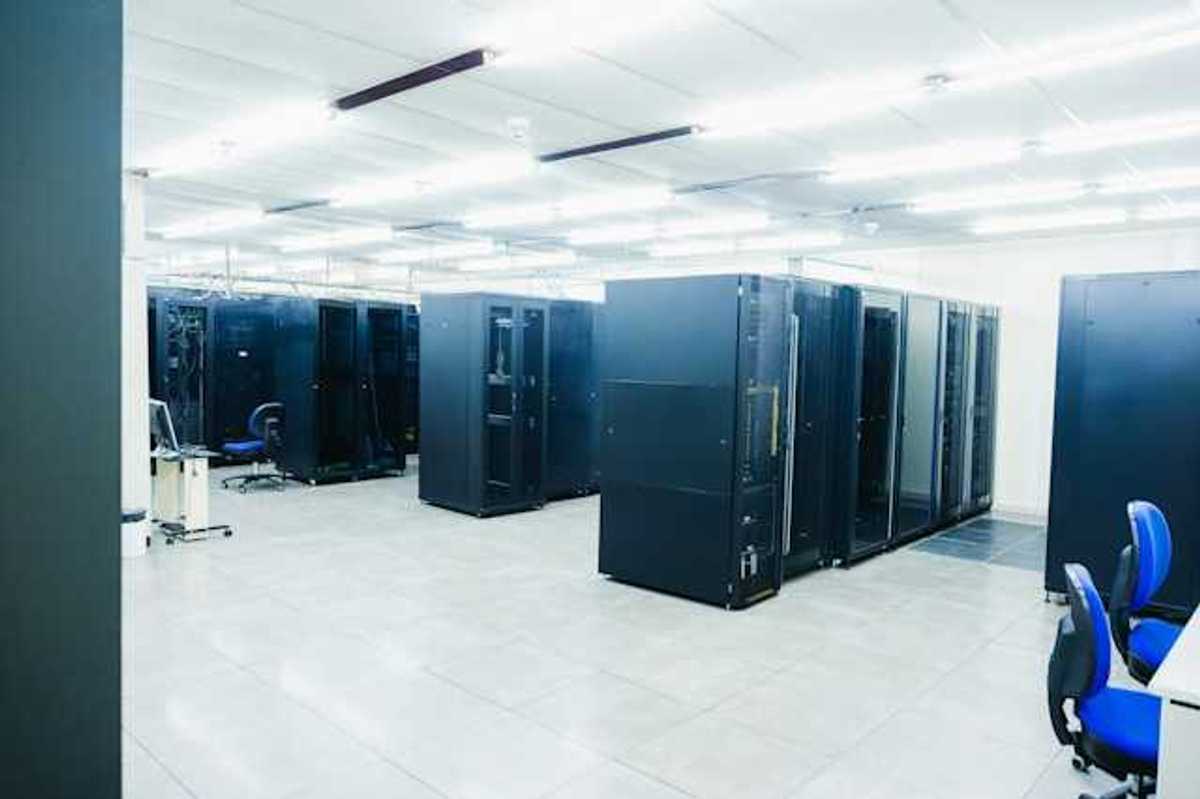 A room full of black server cabinets under fluorescent lighting