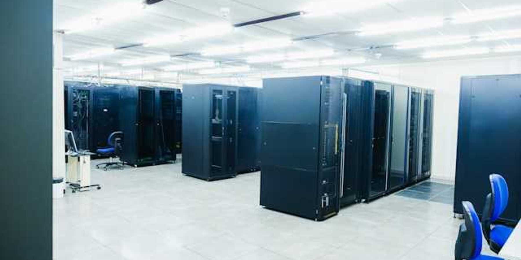 A room full of black server cabinets under fluorescent lighting