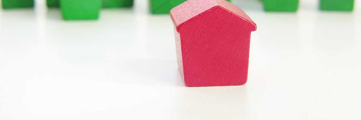 A row of green wooden house models with a red house model in the foreground