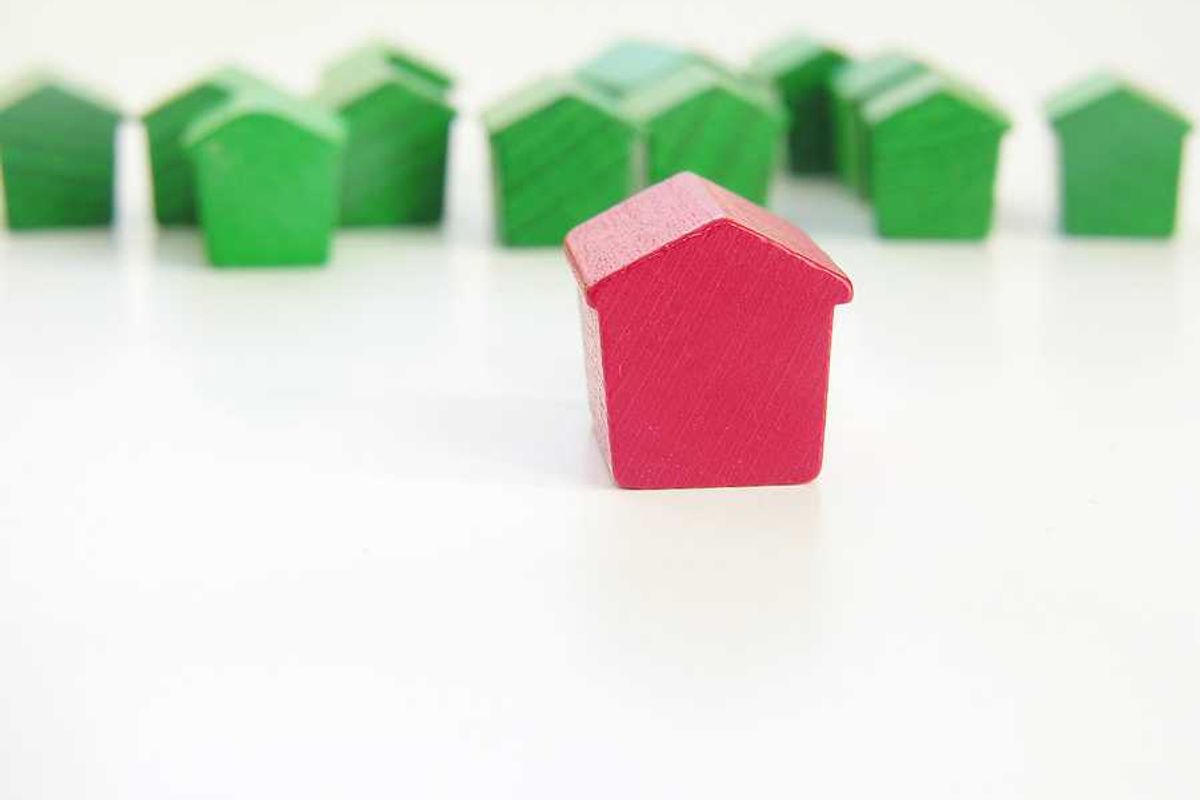 A row of green wooden house models with a red house model in the foreground