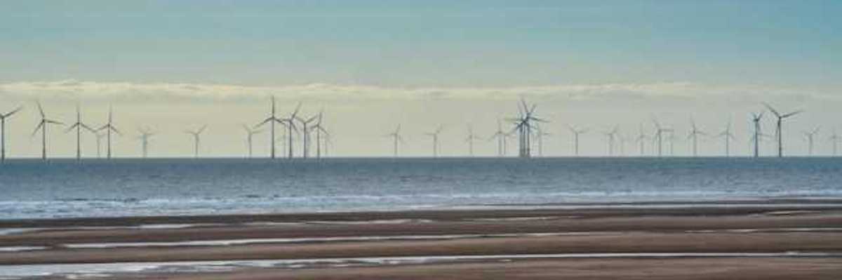 A row of offshore wind turbines viewed from a beach