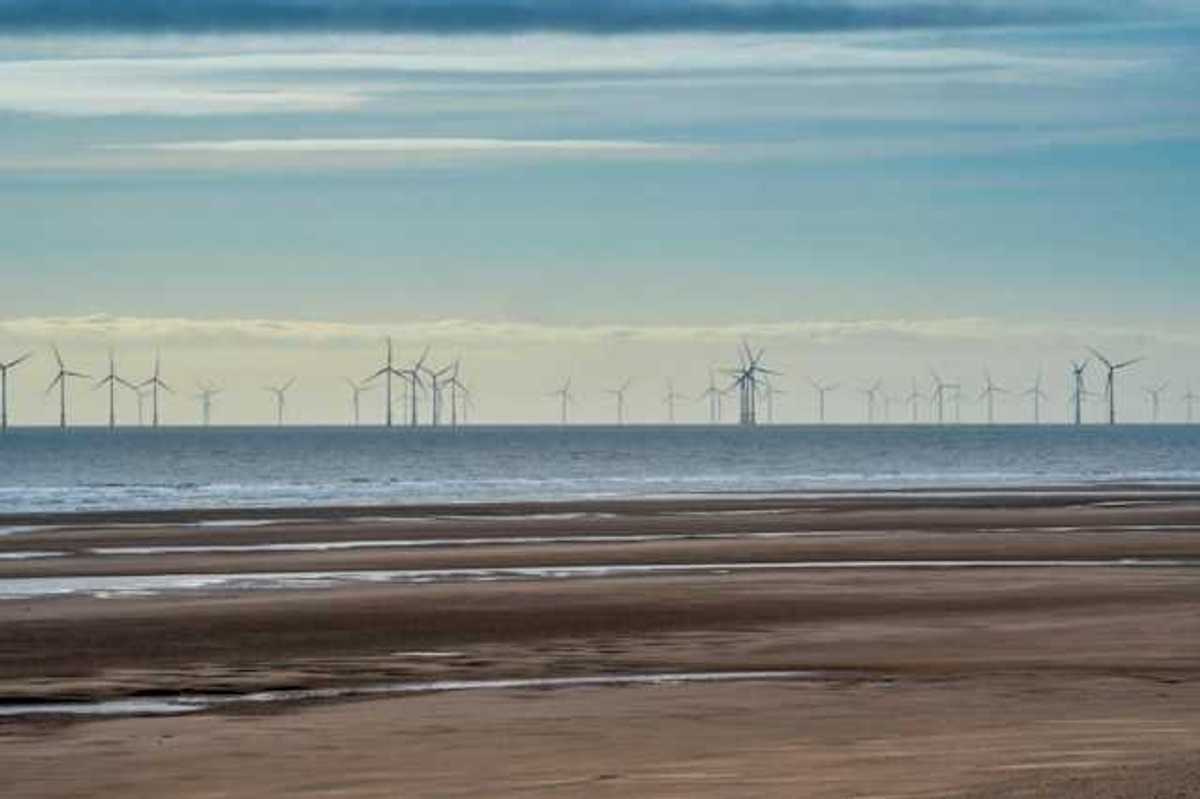 A row of offshore wind turbines viewed from a beach