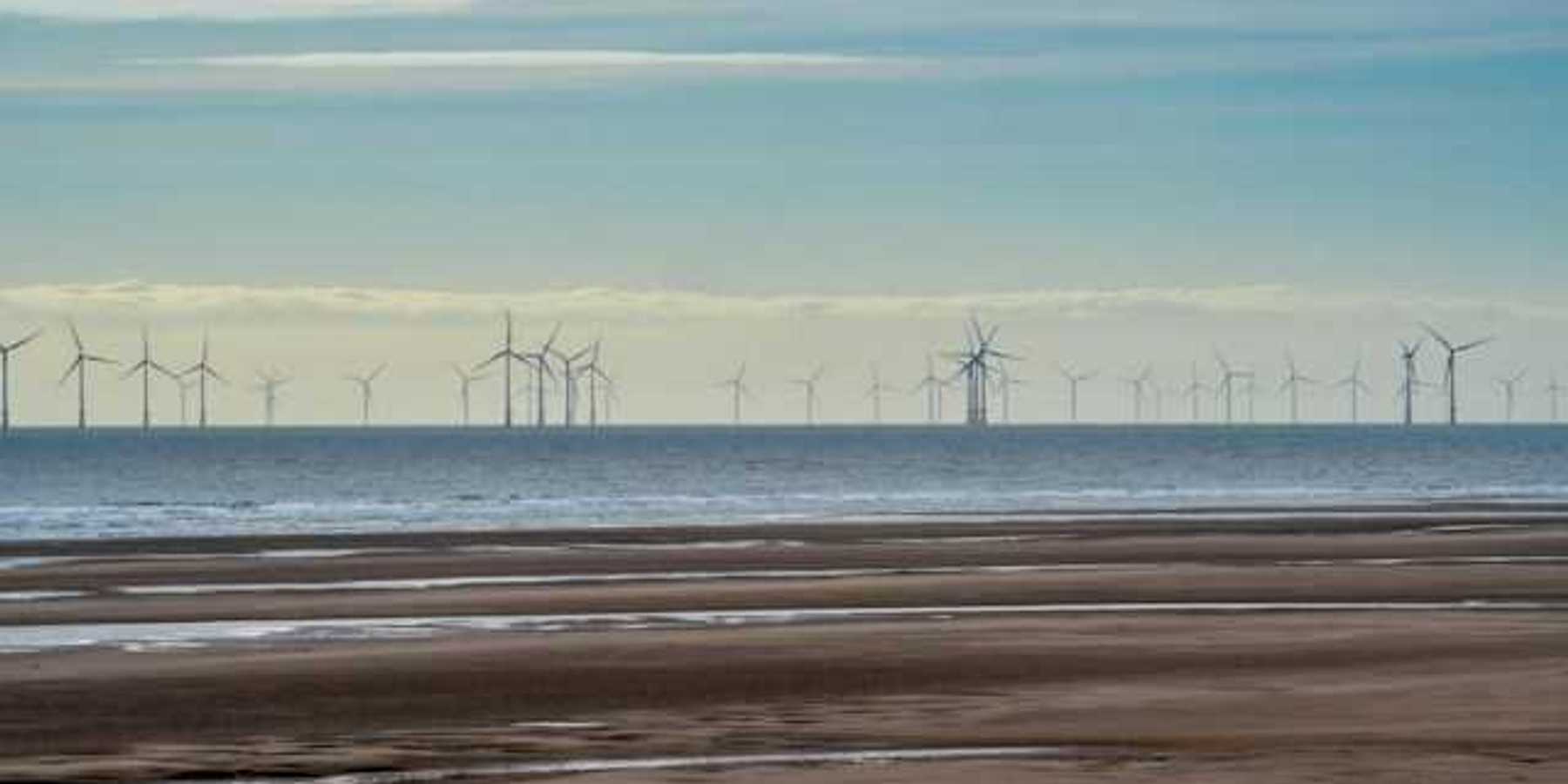 A row of offshore wind turbines viewed from a beach