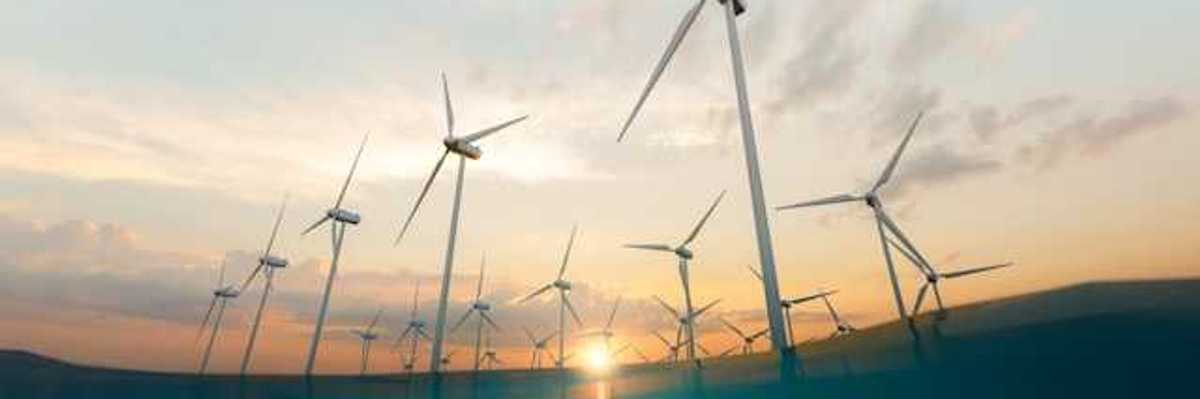 A row of offshore wind turbines with the setting sun in the background