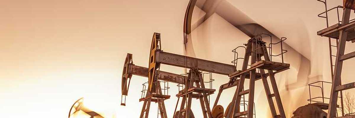 A row of oil and gas pump jacks against a sunset