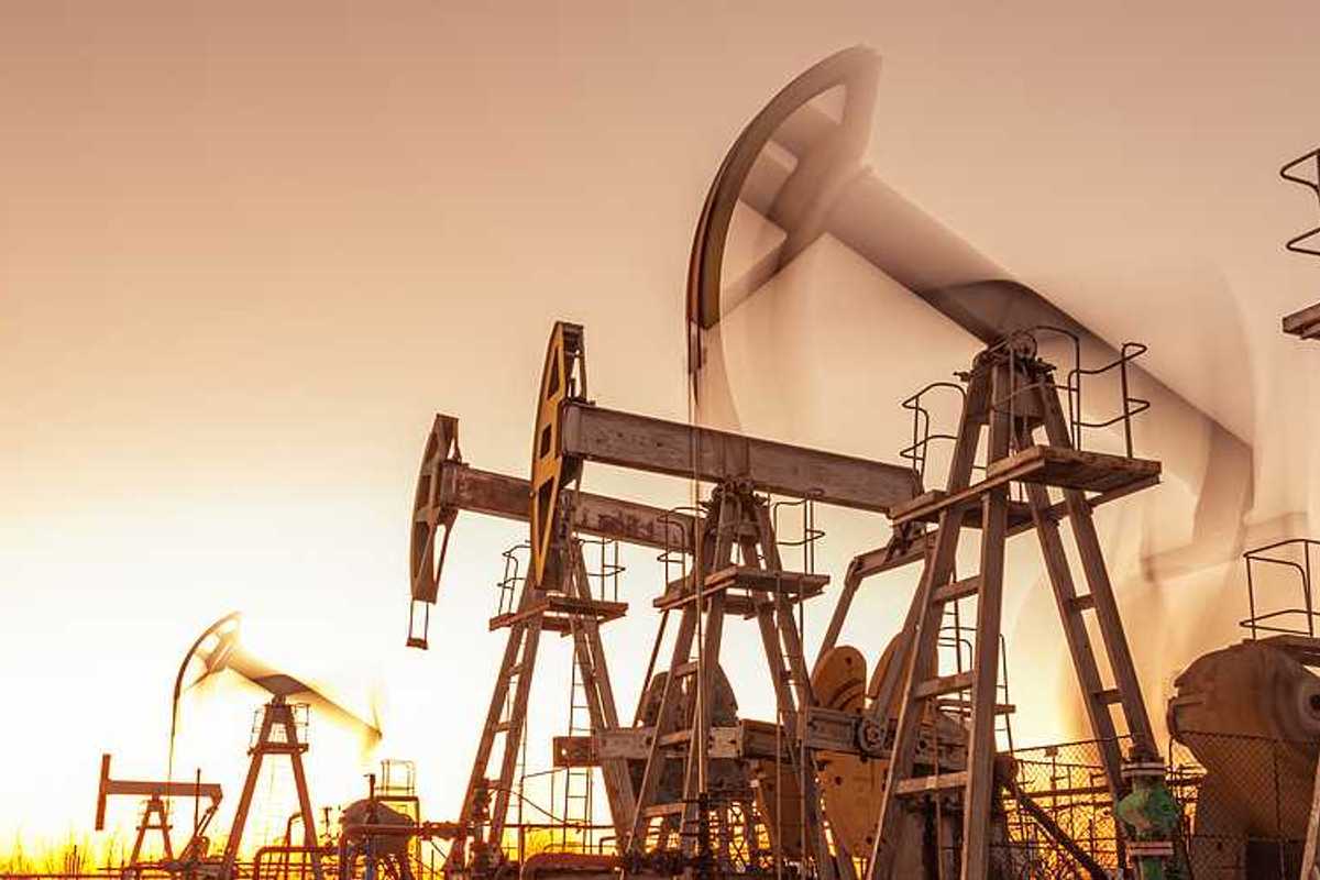 A row of oil and gas pump jacks against a sunset