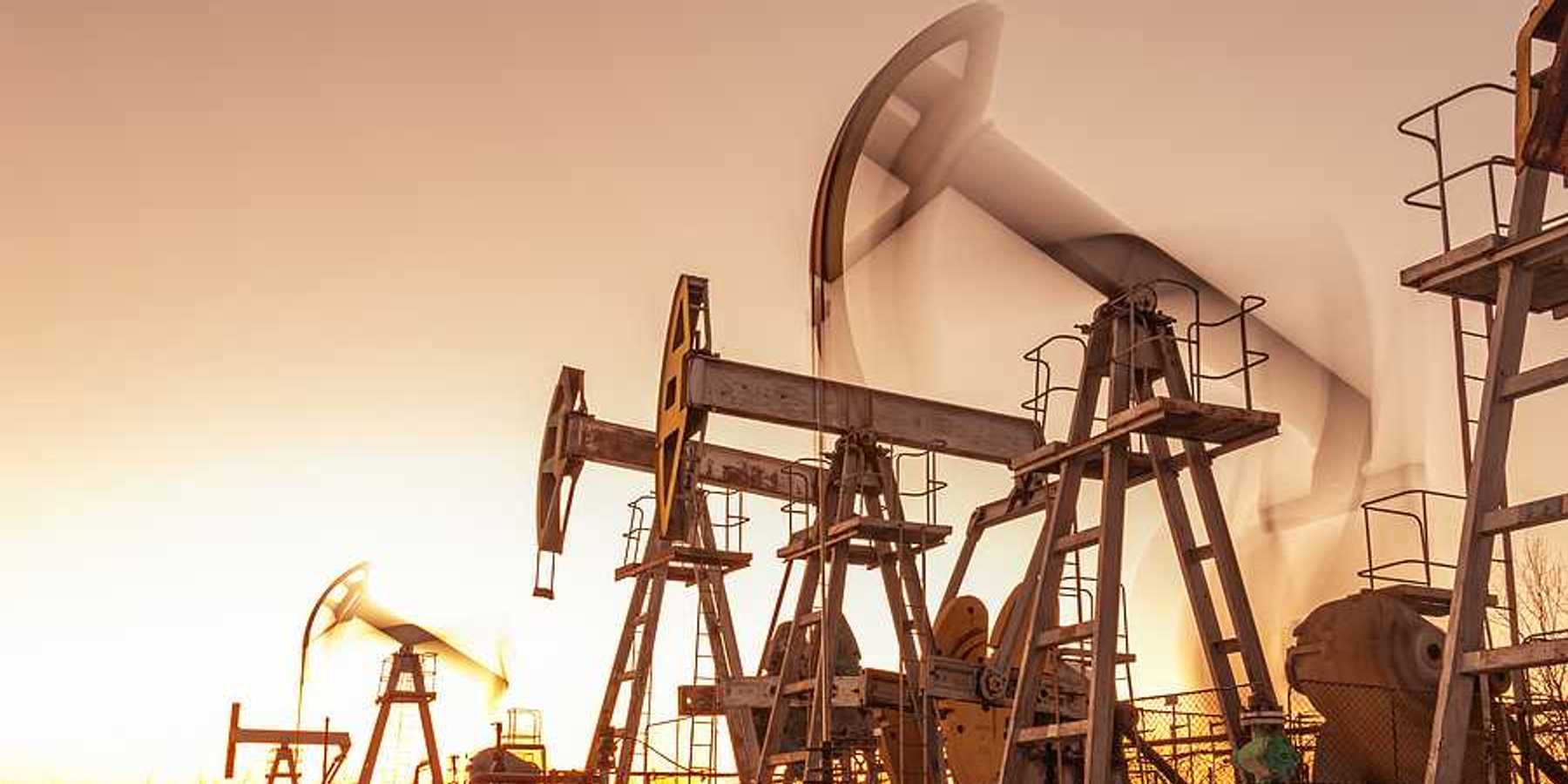 A row of oil and gas pump jacks against a sunset