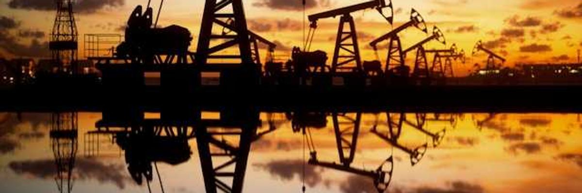 A row of oil drilling pump jacks stretching into the distance at sunset