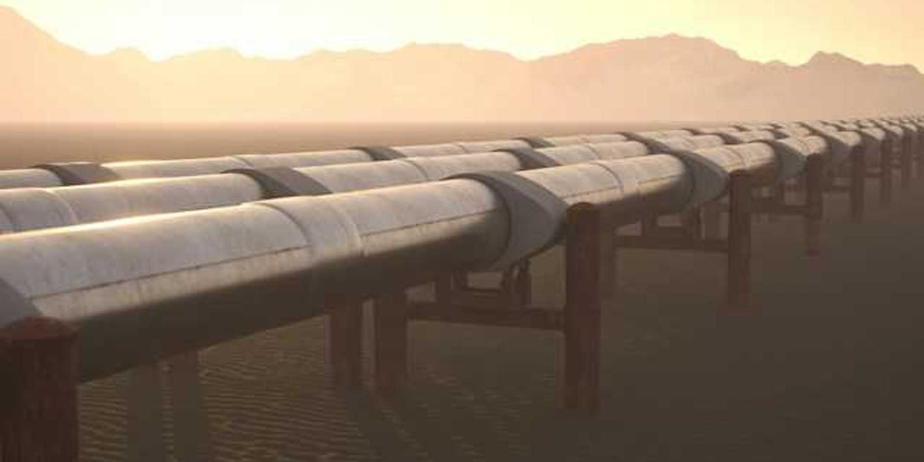A row of pipelines stretching across a dry environment with mountains in the background