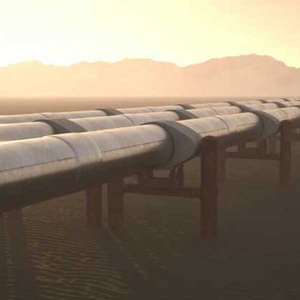 A row of pipelines stretching across a dry environment with mountains in the background