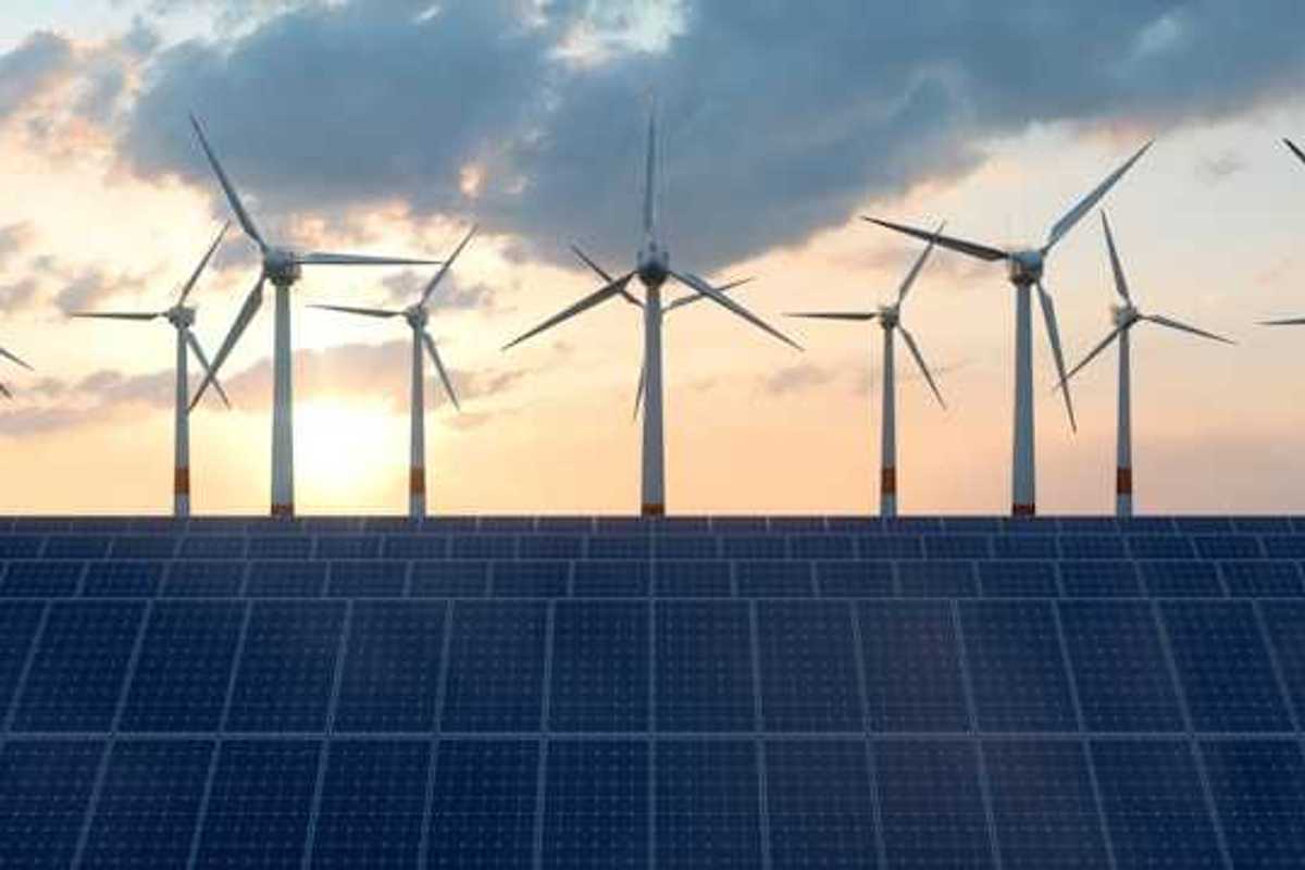 A row of solar panels in the foreground with wind turbines in the background
