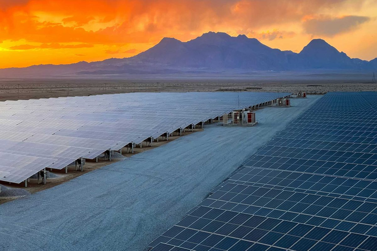 a row of solar panels sitting on top of desert land with mountains and sunset in background.