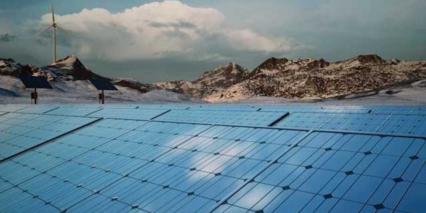 A row of solar panels with mountains and a wind turbine in the background