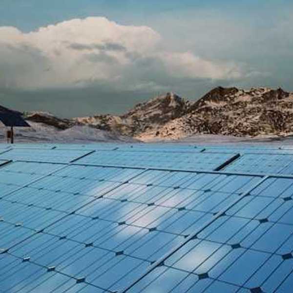A row of solar panels with mountains and a wind turbine in the background