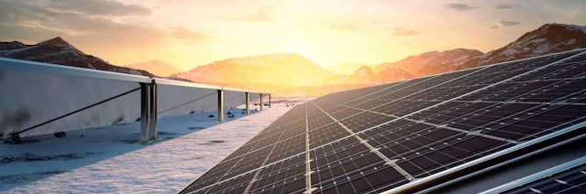 A row of solar panels with the setting sun and a mountain range in the background