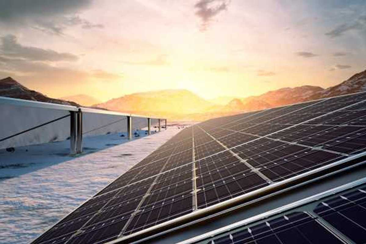 A row of solar panels with the setting sun and a mountain range in the background