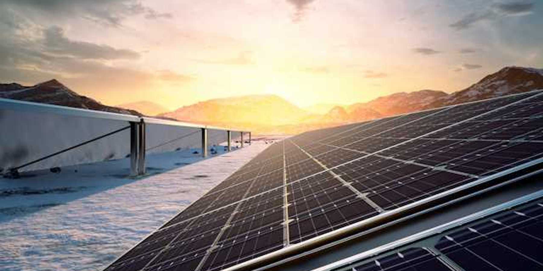 A row of solar panels with the setting sun and a mountain range in the background