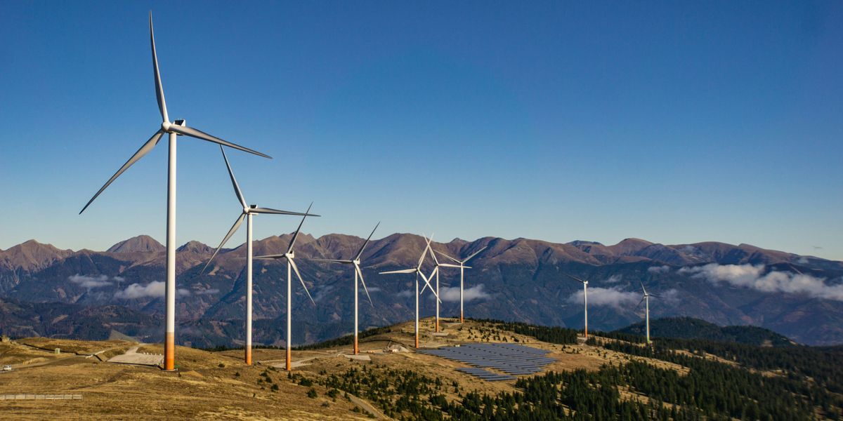 A row of wind turbines and solar panels on a mountainside.