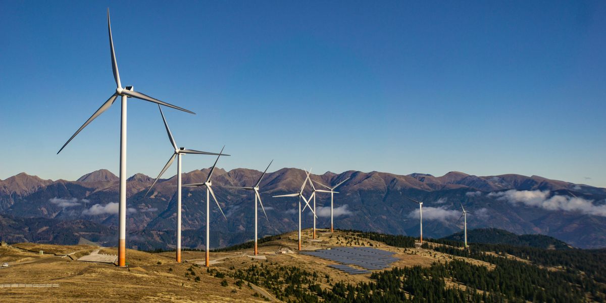 A row of wind turbines and solar panels on a mountainside.