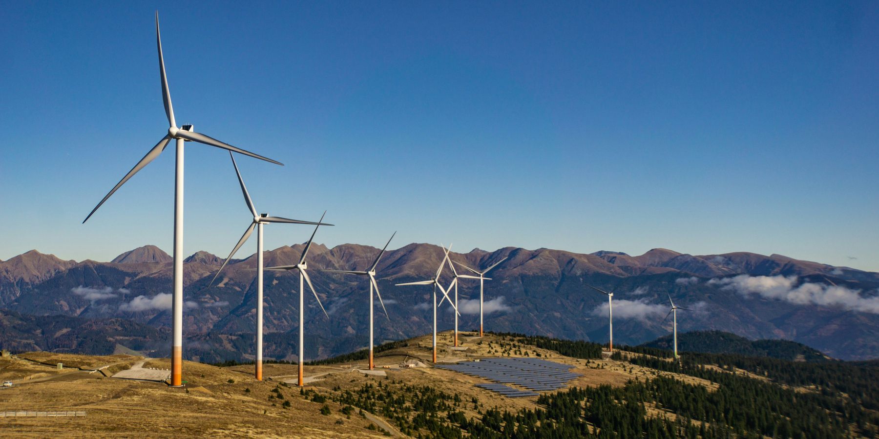 A row of wind turbines and solar panels on a mountainside.