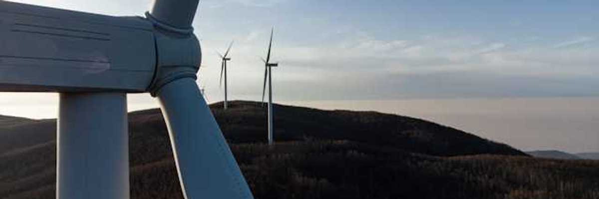 A row of wind turbines at dusk installed on rolling hills