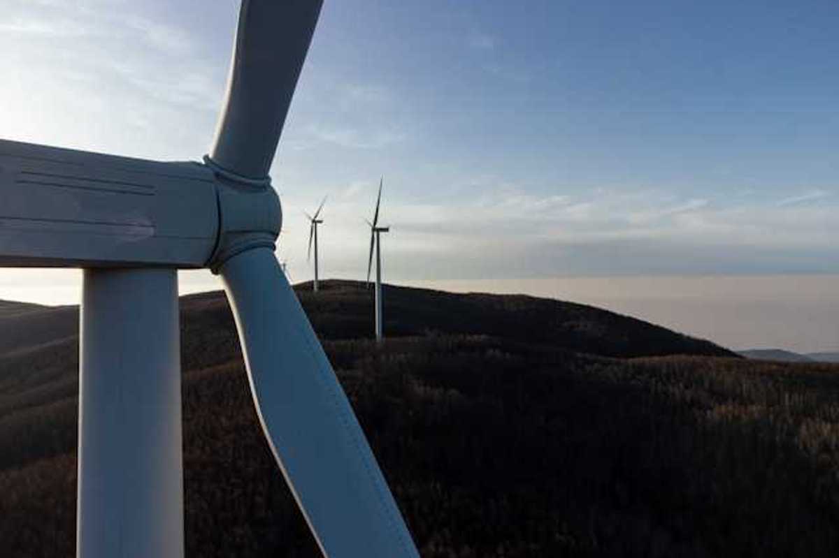 A row of wind turbines at dusk installed on rolling hills
