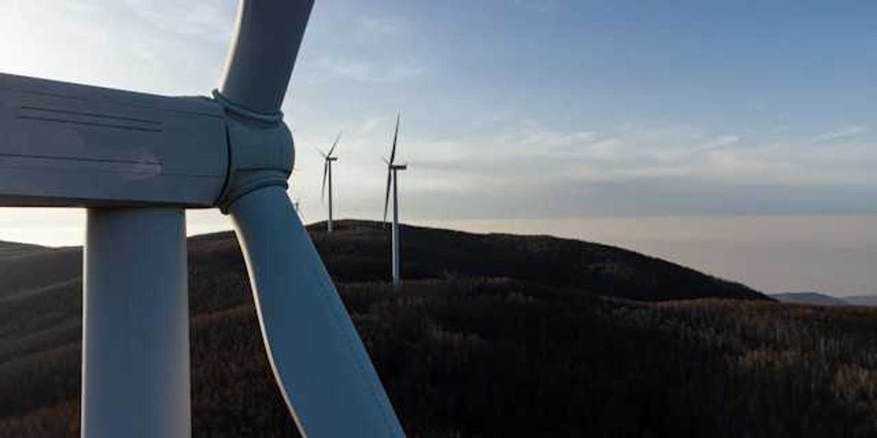 A row of wind turbines at dusk installed on rolling hills