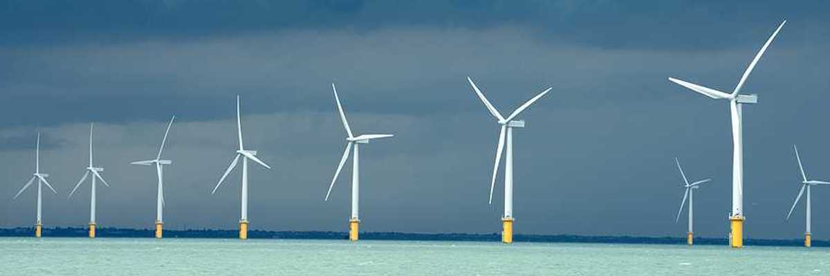 A row of wind turbines in the ocean with dark storm clouds in the distance