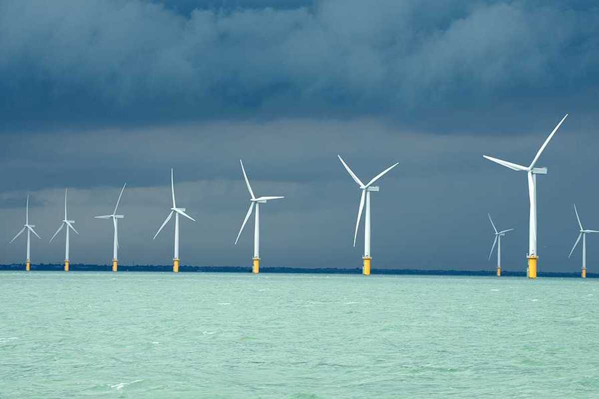 A row of wind turbines in the ocean with dark storm clouds in the distance