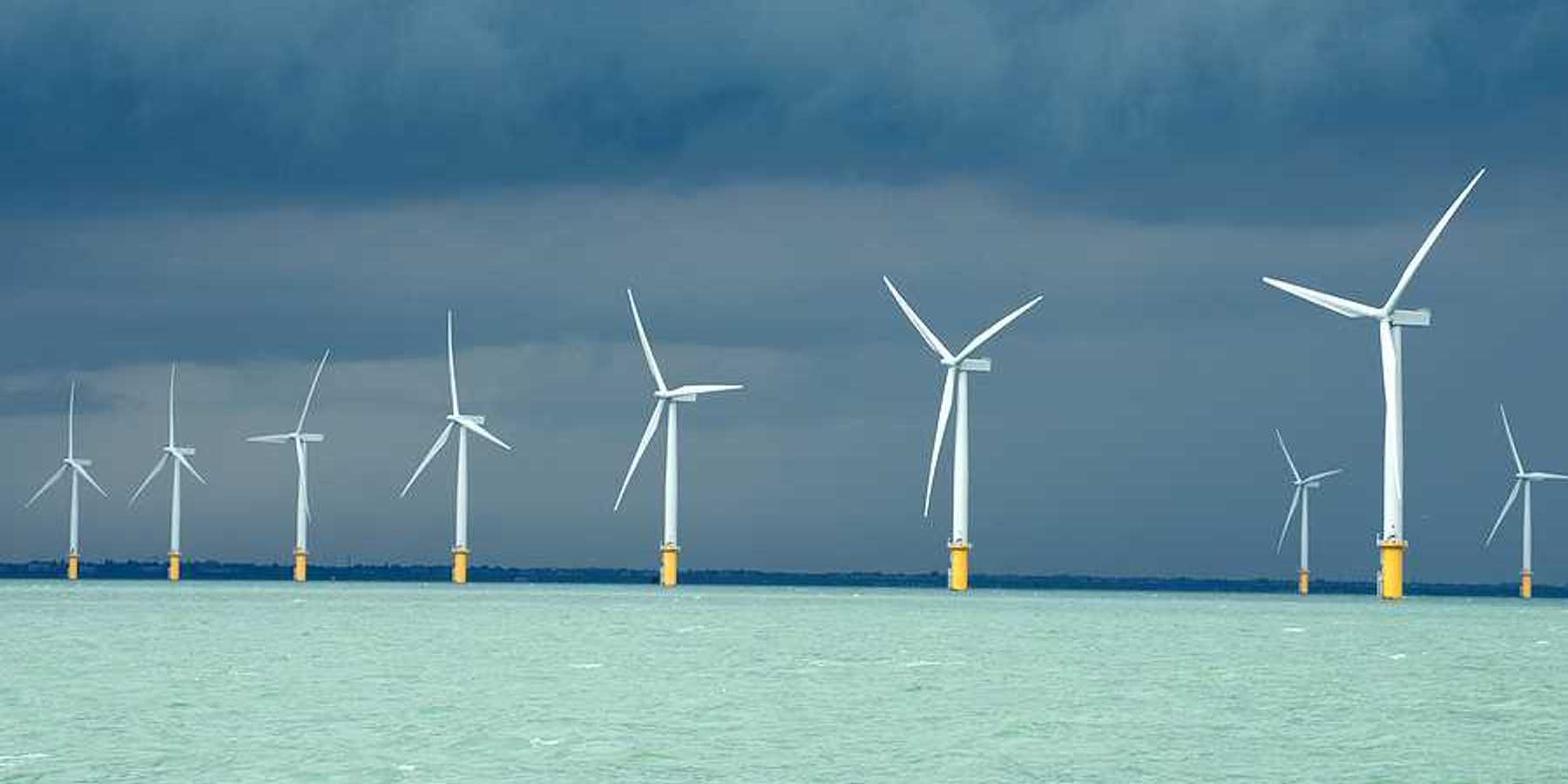 A row of wind turbines in the ocean with dark storm clouds in the distance