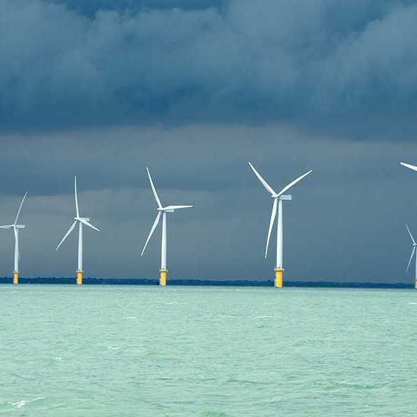 A row of wind turbines in the ocean with dark storm clouds in the distance