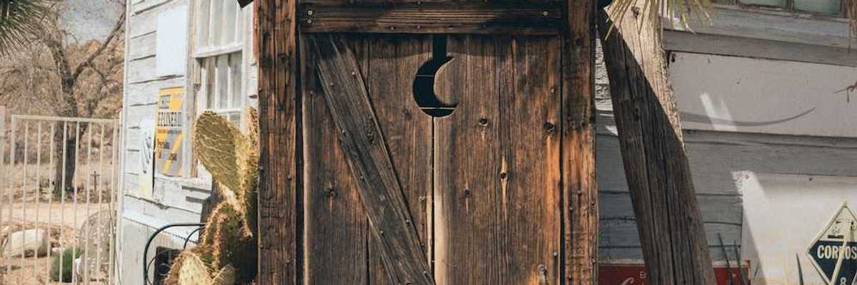 A rustic outhouse with a crescent moon in the door