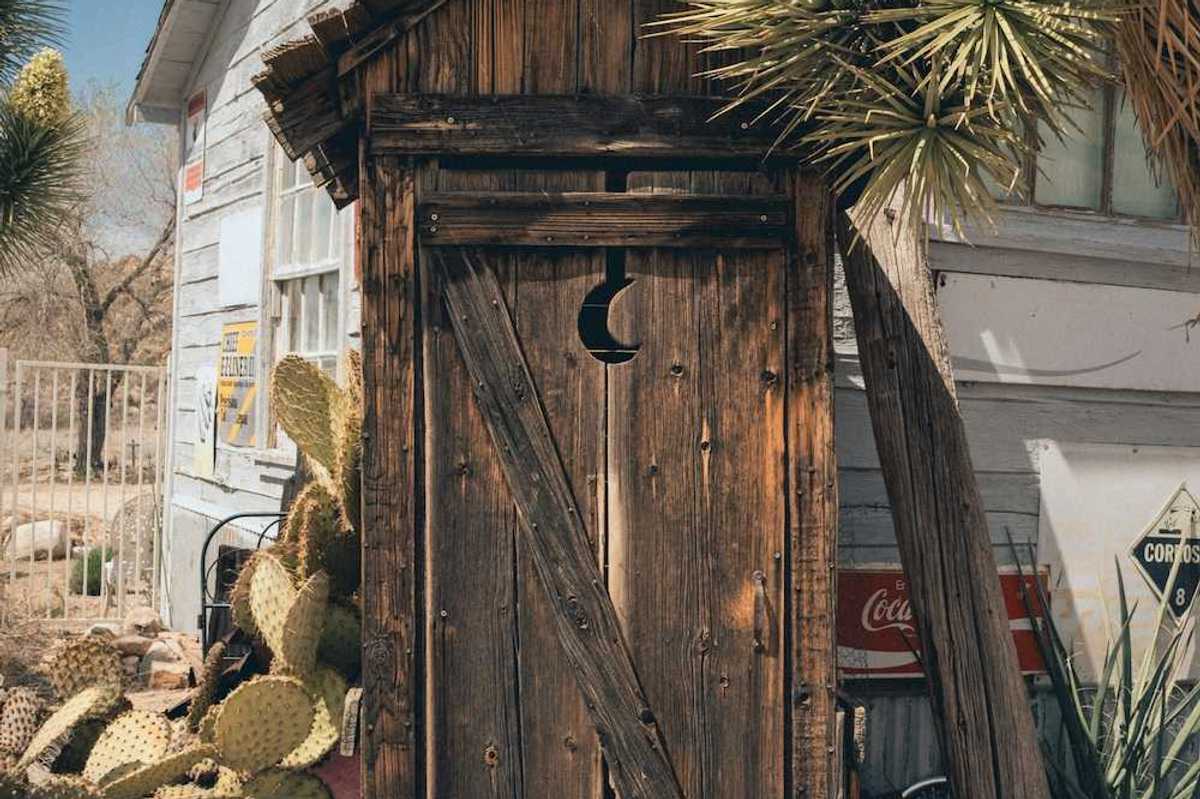 A rustic outhouse with a crescent moon in the door