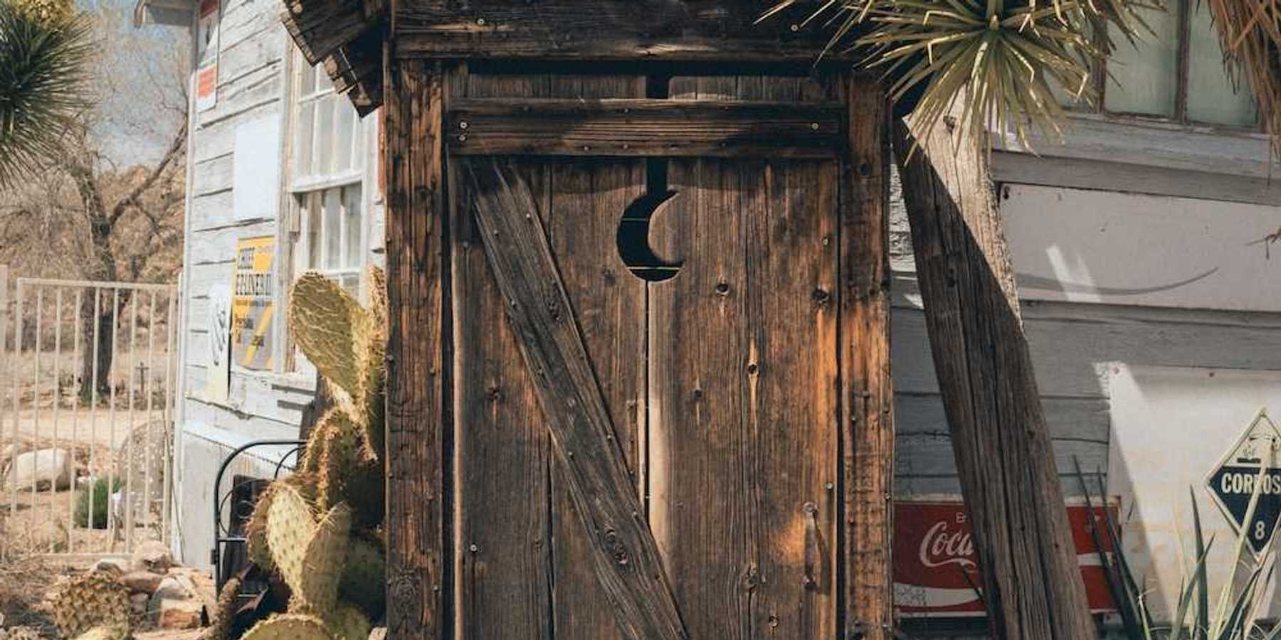A rustic outhouse with a crescent moon in the door