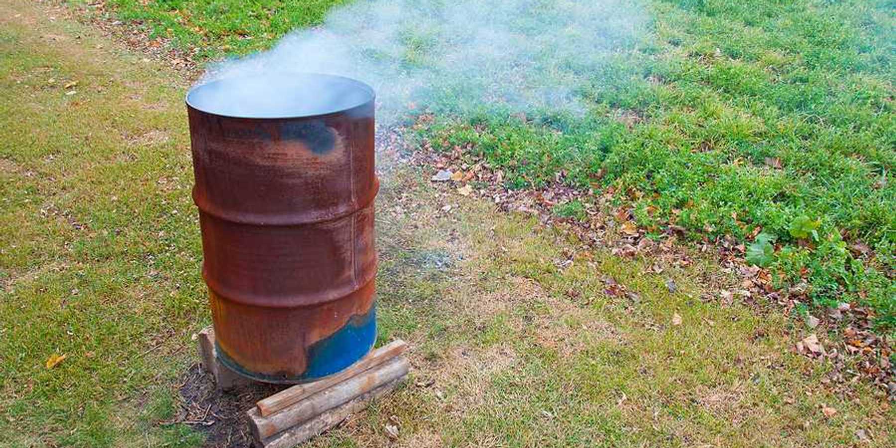 A rusty barrel with burning items in it, smoke billowing from the top