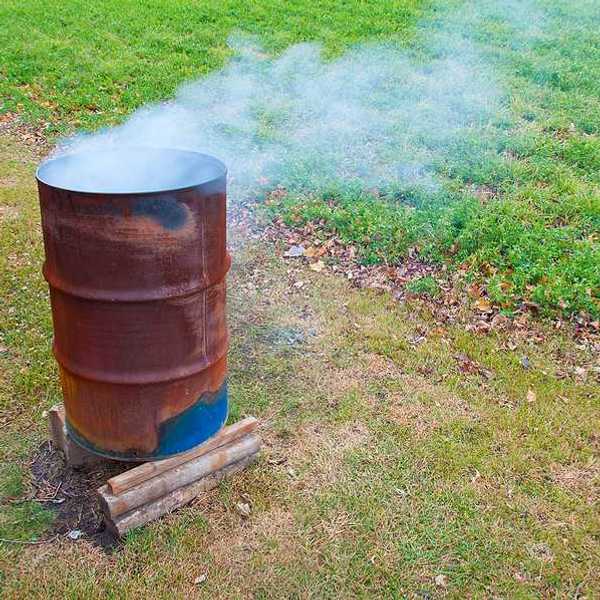 A rusty barrel with burning items in it, smoke billowing from the top