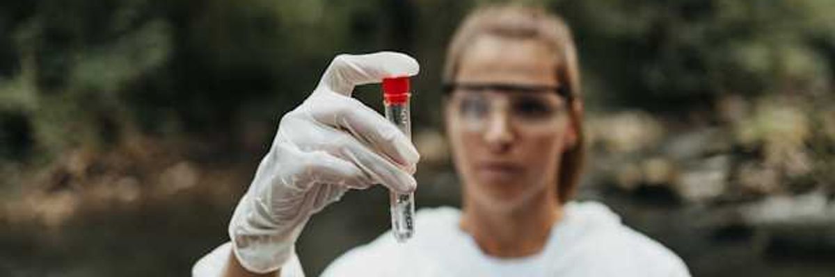A scientist standing in a stream holding a container with a water sample