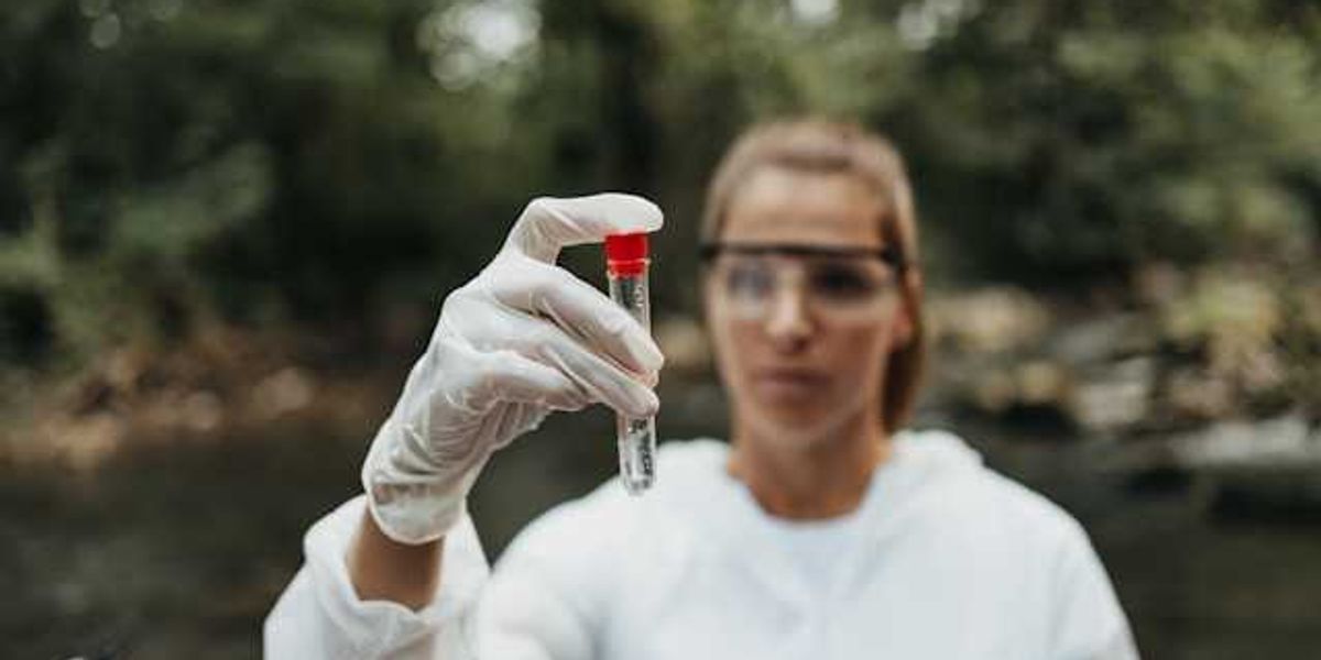 A scientist standing in a stream holding a container with a water sample