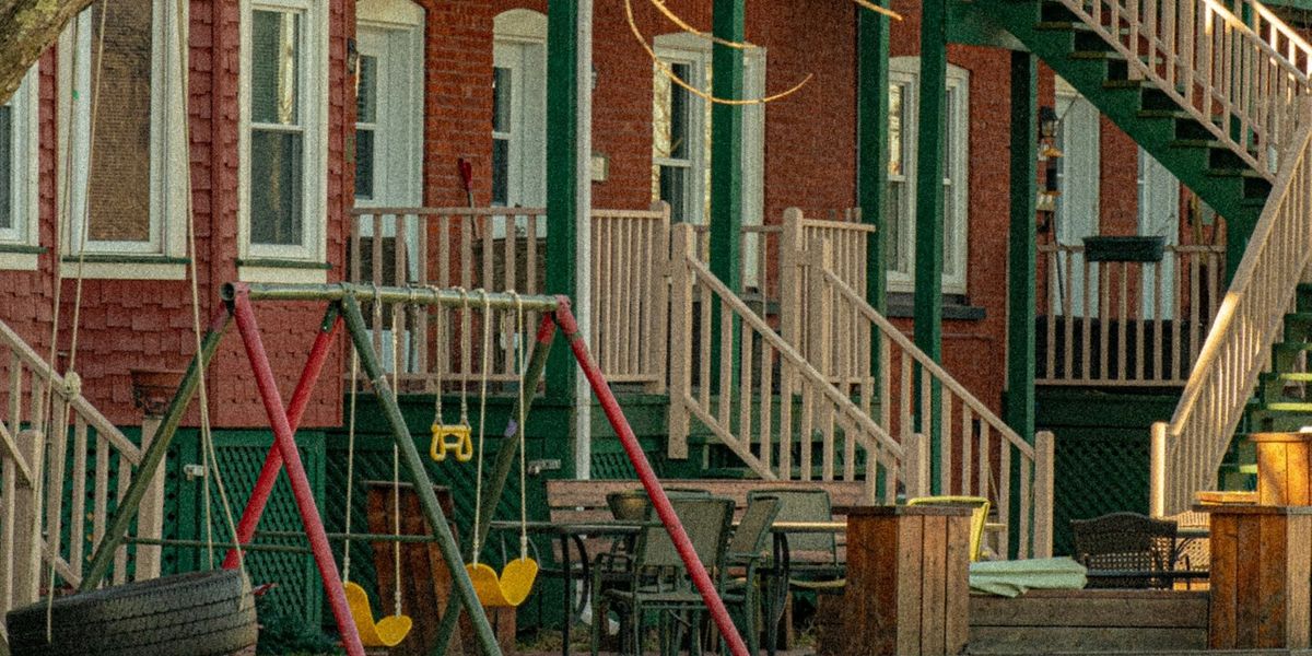 A series of row houses with stairs leading to porches and a swing set in the front yard.