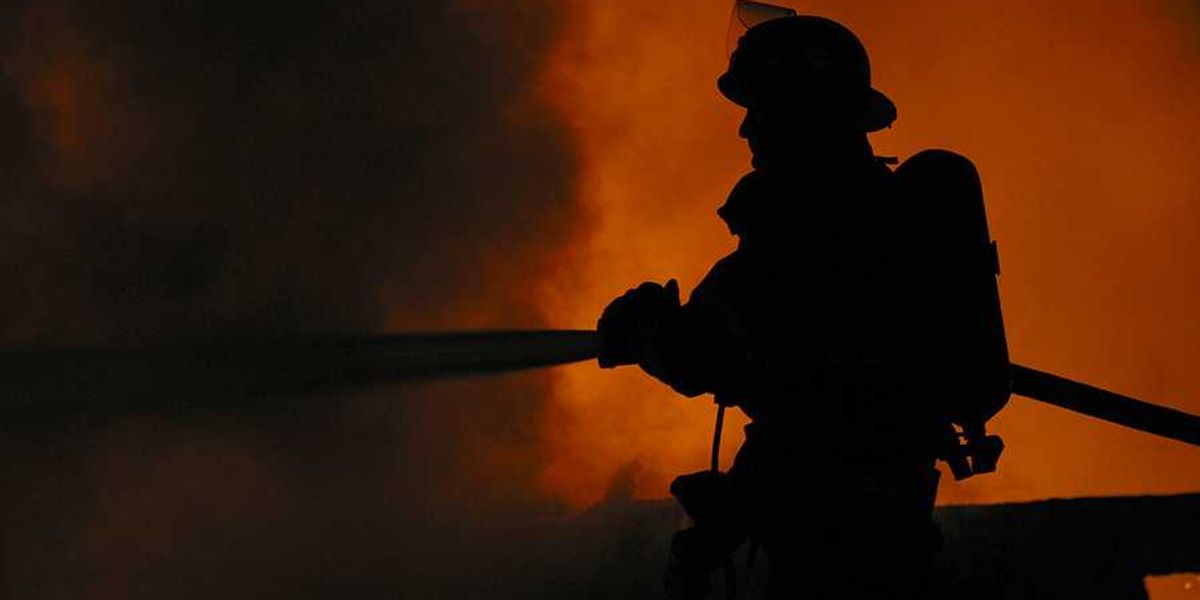 A silhouette of a firefighter spraying water on a fire with billowing smoke