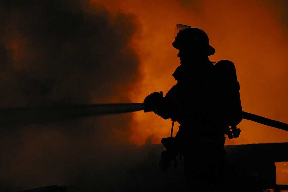 A silhouette of a firefighter spraying water on a fire with billowing smoke